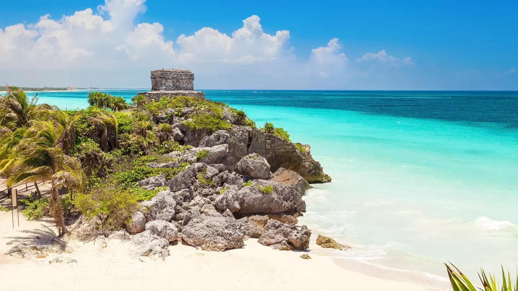 Cozumel beach view featuring Tulum's God of Wind temple ruins atop rocky cliffs, turquoise waters, and palm trees, ideal for Royal Caribbean cruise exploration.